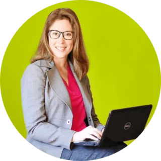 author Amanda L. Grossman on laptop, with green background, wearing glasses and business suit